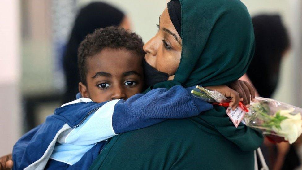 A woman carries a child as people fleeing conflict in Sudan arrive at an airport in Abu Dhabi after an evacuation flight, on April 29, 2023