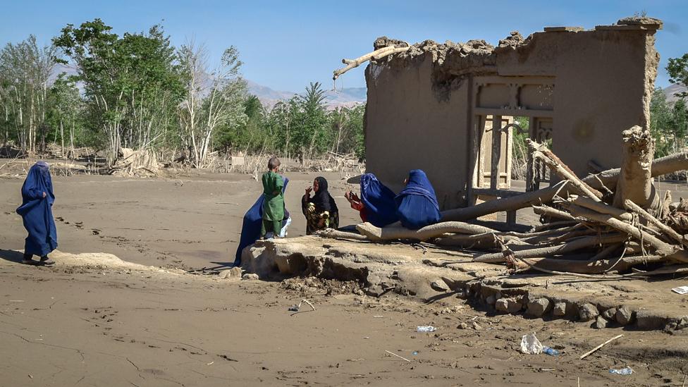 A family sits in front of the remains of a building