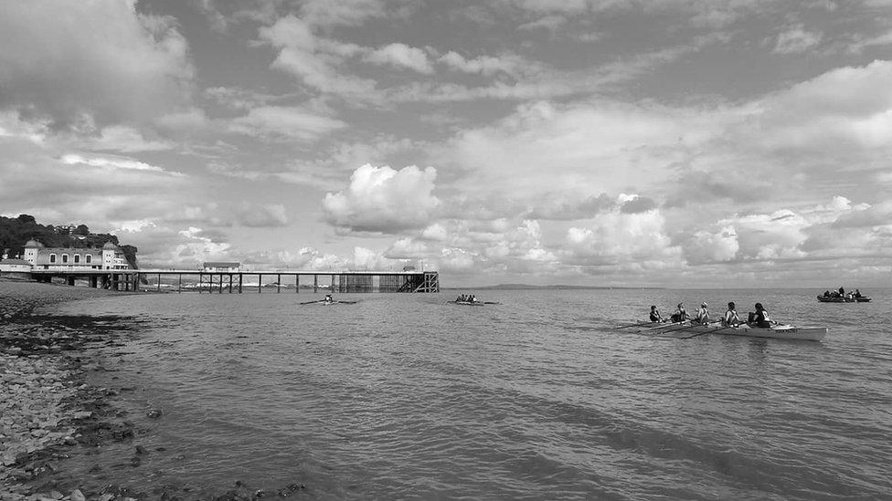 Rowers in the sea off Penarth, with the pier in the background - a black and white image