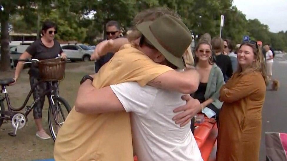 Two people hug over a barricade as others watch on