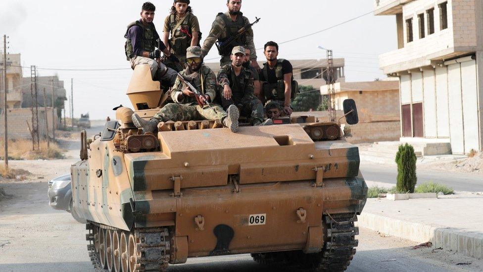 Turkish-backed Syrian rebel fighters sit on an armoured vehicle in Tal Abyad, Syria (21 October 2019)