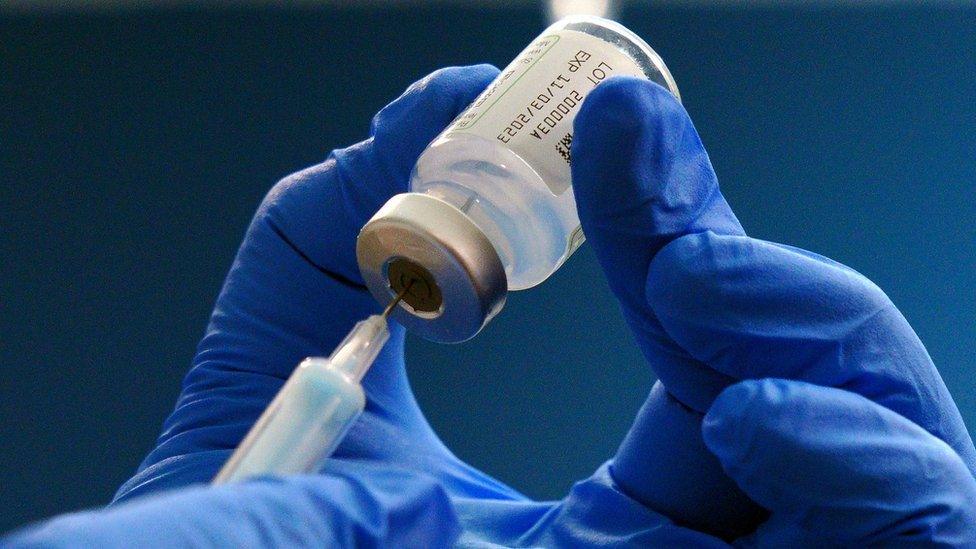 A nurse prepares a covid booster jab. A syringe is being placed into a bottle by someone wearing protective gloves.