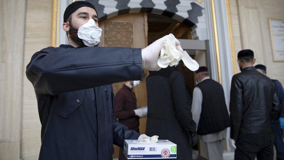 Volunteers in face masks hand out gloves at the entrance to the Heart of Chechnya Mosque in Grozny, Chechen Republic