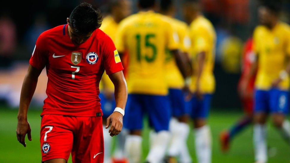 Alexis Sanchez walks away from a group of Brazil players, looking downcast.