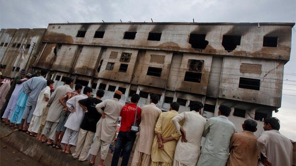 Residents stand outside a garment factory that caught fire the day before, in Karachi September 13, 2012.