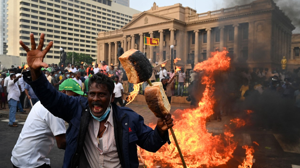 A man with bread loafs on a stave protests with others outside the president's office in Colombo