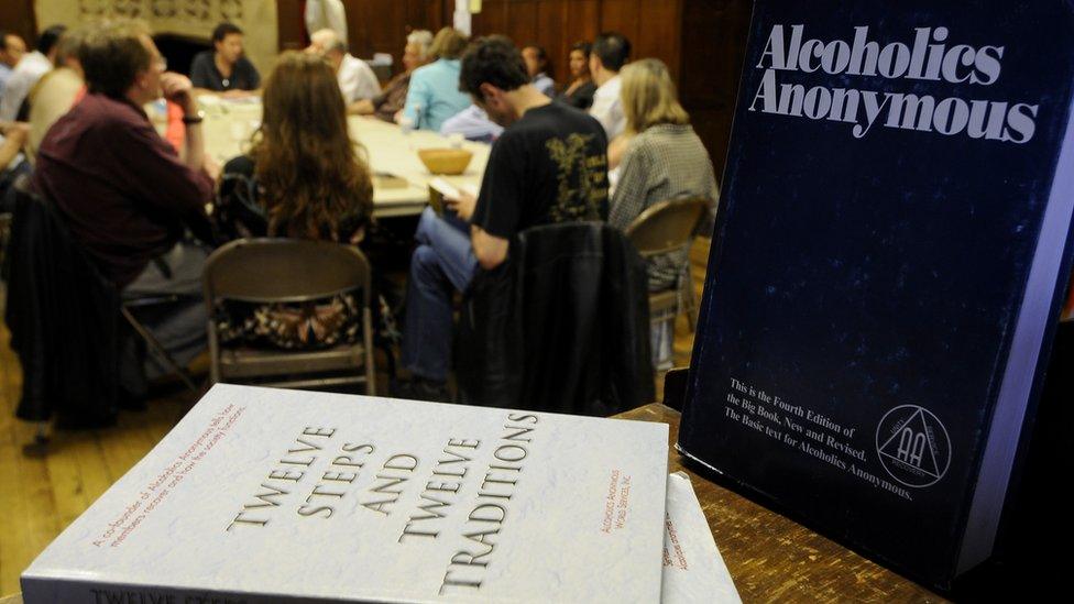 A group of people attend and AA meeting with AA literature in the foreground