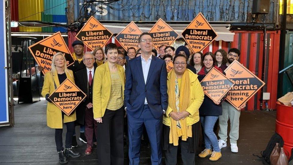 Mr Blackie stands in front of a small crowd of supporters holding orange party signs