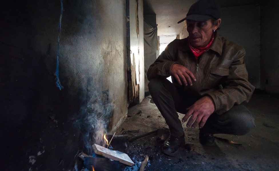 Derrick Brown crouches over trying to get a fire started to make coffee for himself and a friend in the derelict San Jose building in Johannesburg, South Africa