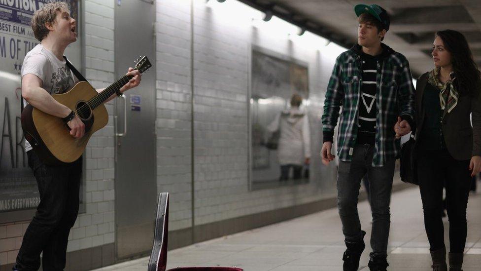 Busker on London Undergound with two people walking past