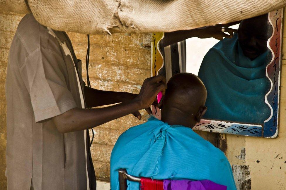 A man looks in the mirror while a barber shaves his head