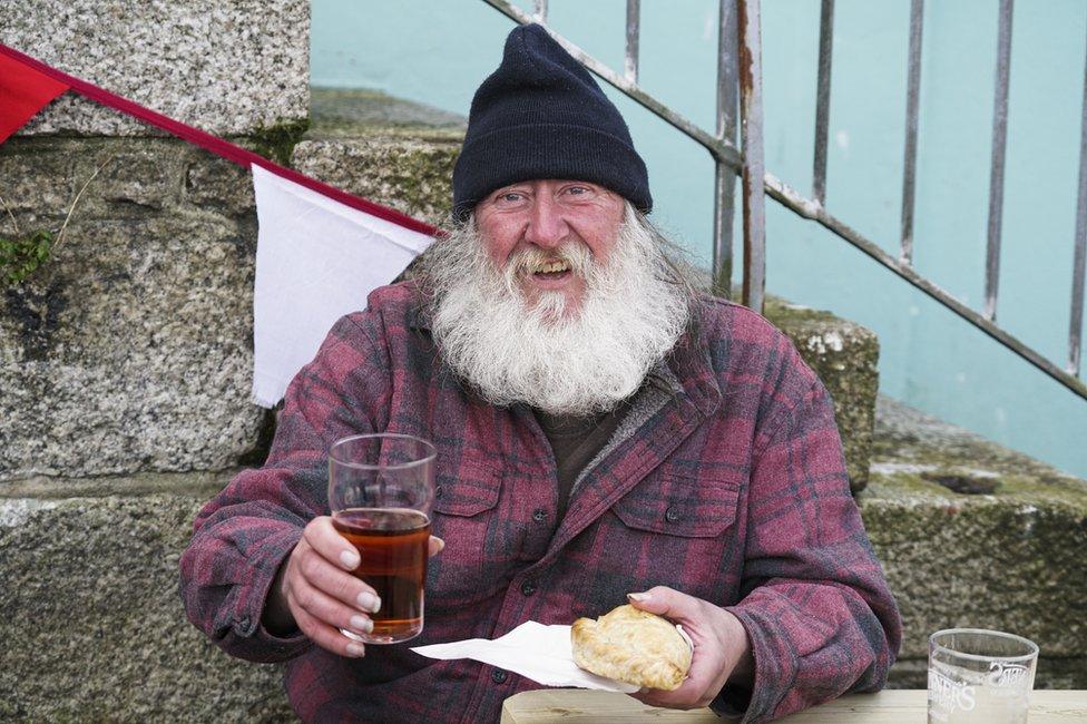 A man holds a pint of beer and a pasty