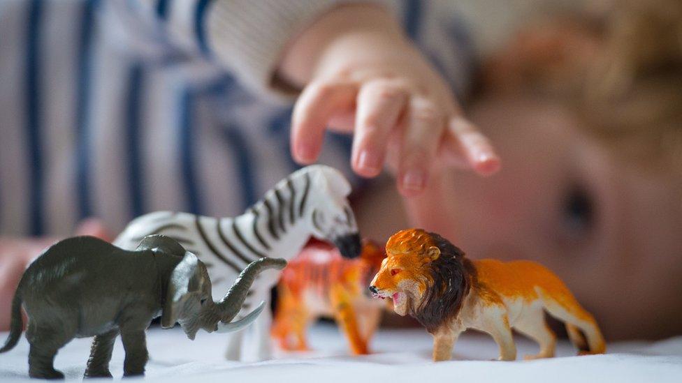 A pre-school age child playing with plastic toy animals