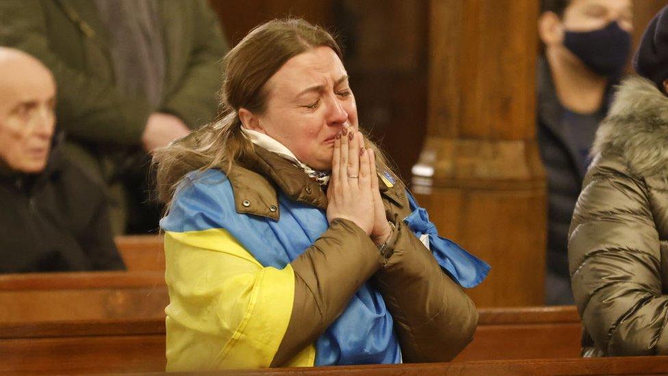 A woman draped in a Ukraine flag prays in Ukrainian Catholic Cathedral