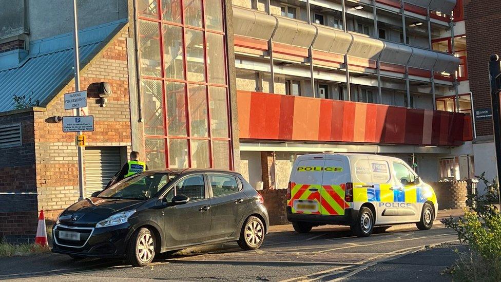 A car and police van parked on the street outside a block of flats