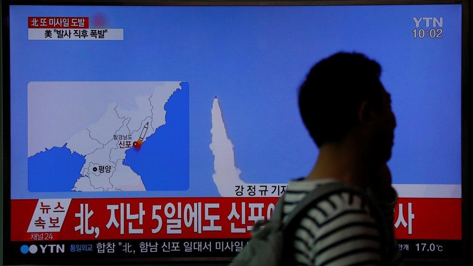 Passenger at railway station in Seoul walks past TV news report of failed missile launch