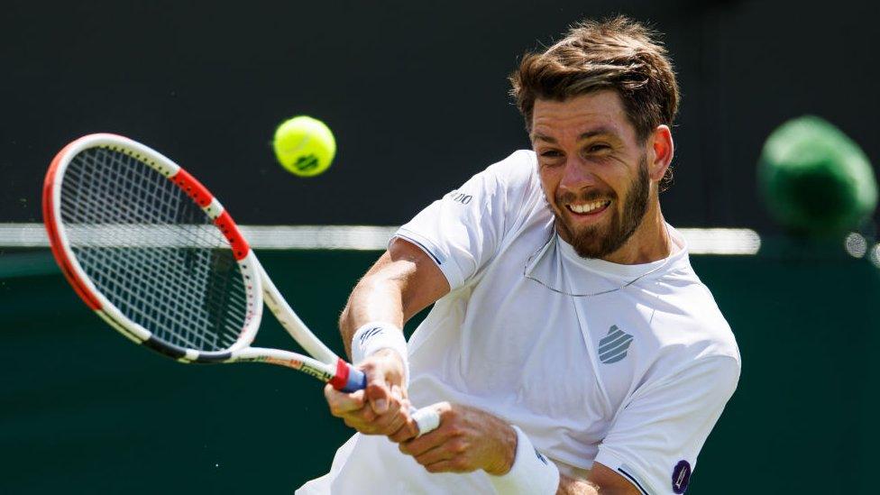 still shows cameron norrie using both hands to bring his tennis racket forward to hit a flying tennis ball