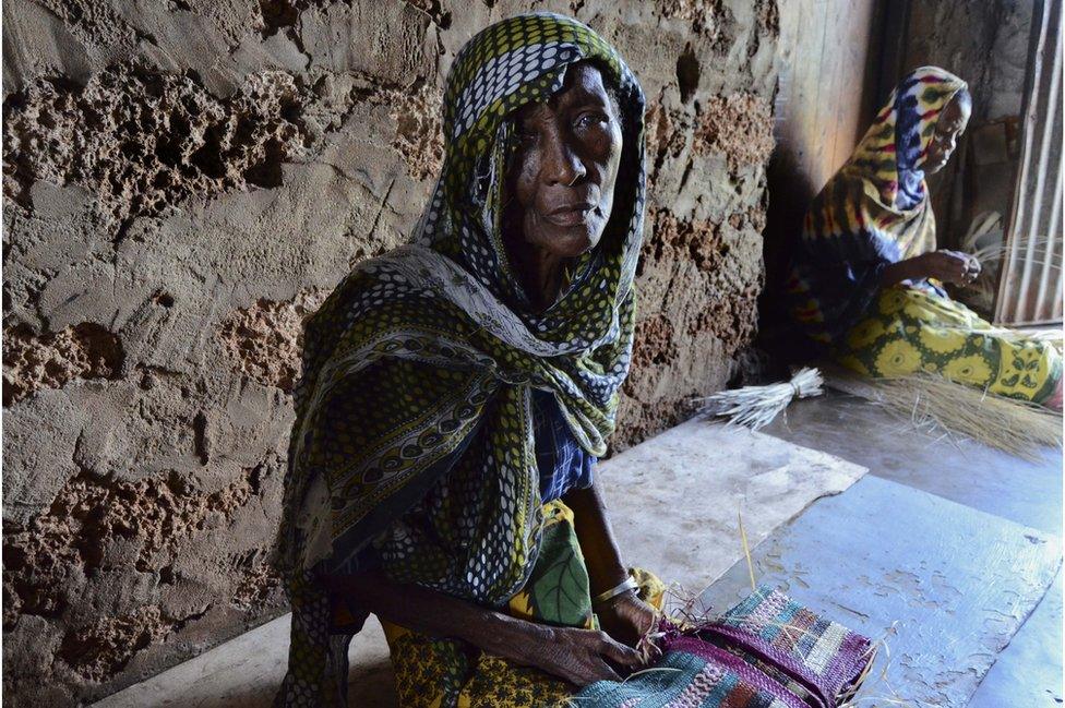 A woman in a headscarf sits on her bed.