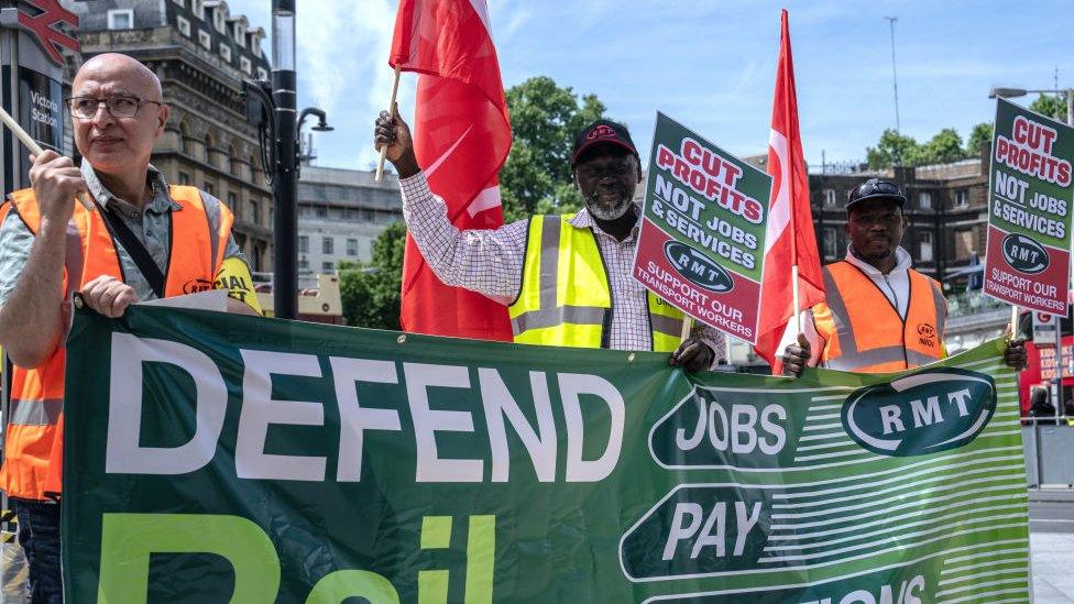 RMT union members in hi-vis vests hold placards as they picket outside Victoria train station