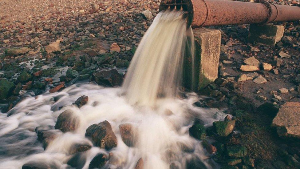 Effluent river waste from a rusty pipe onto a river bank