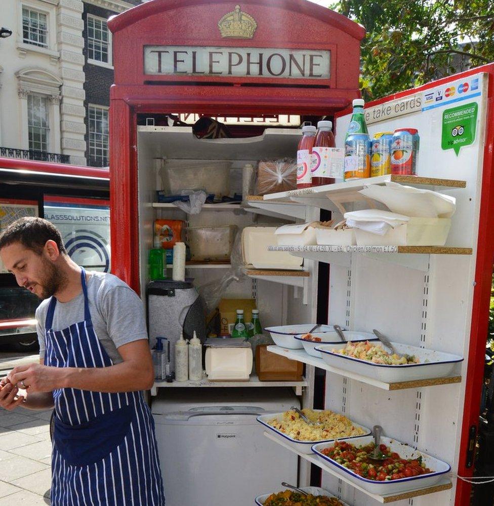 A phone box containing a fridge and various salad items for sale