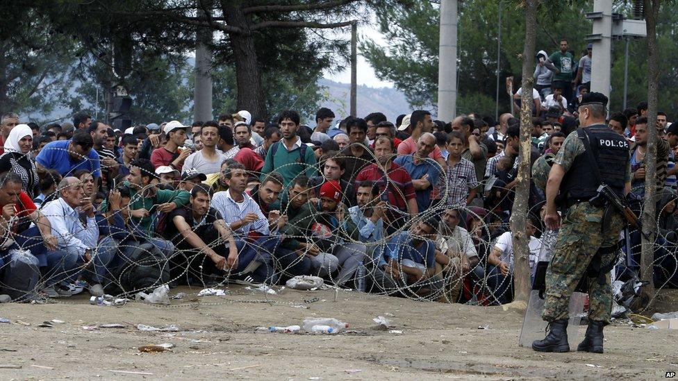 Migrants stand behind the barbed wire, lain by Macedonian police to stop thousands of migrants entering Macedonia illegally from Greece on 22 August 2015