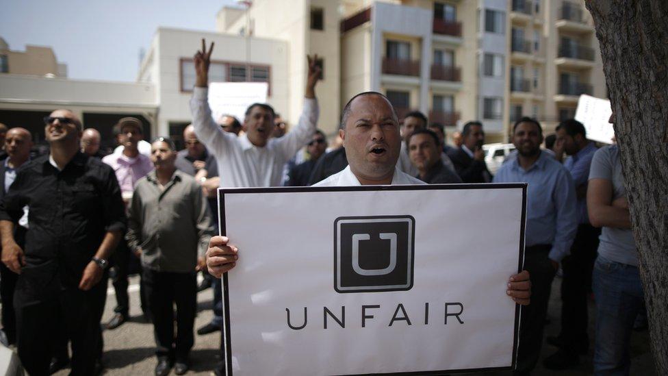 A man holds a sign saying "Uber Unfair" at a protest in California