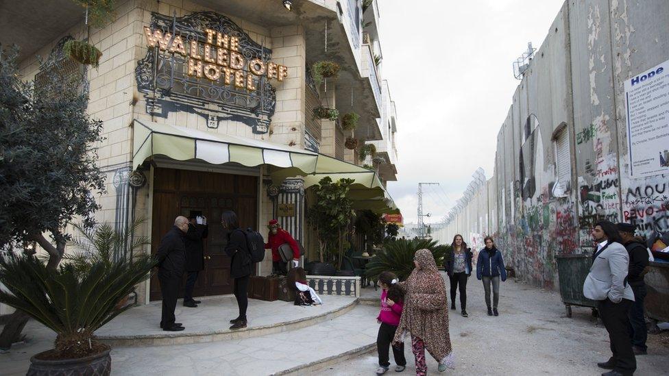 People pass by the "The Walled Off Hotel" and the Israeli security barrier in the West Bank city of Bethlehem, Friday, March 3, 2017.