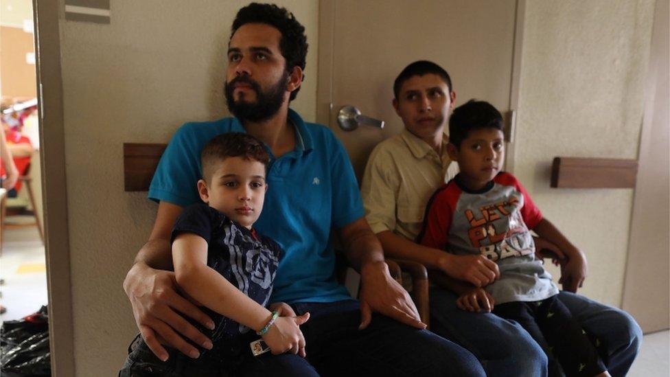 Migrant fathers and their sons sit in a facility after being reunited