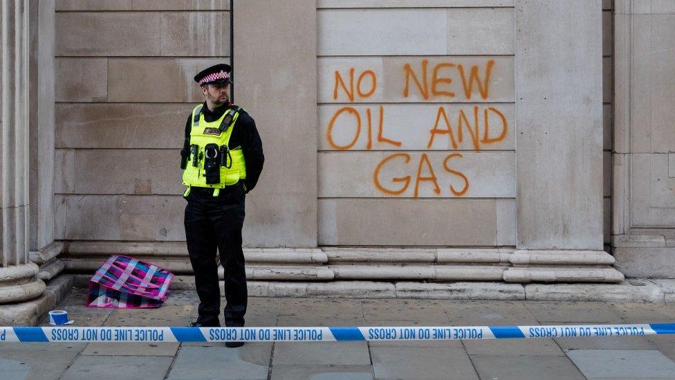 A police officer stands outside graffiti that reads 'no new oil and gas' on the wall of the Bank of England in London