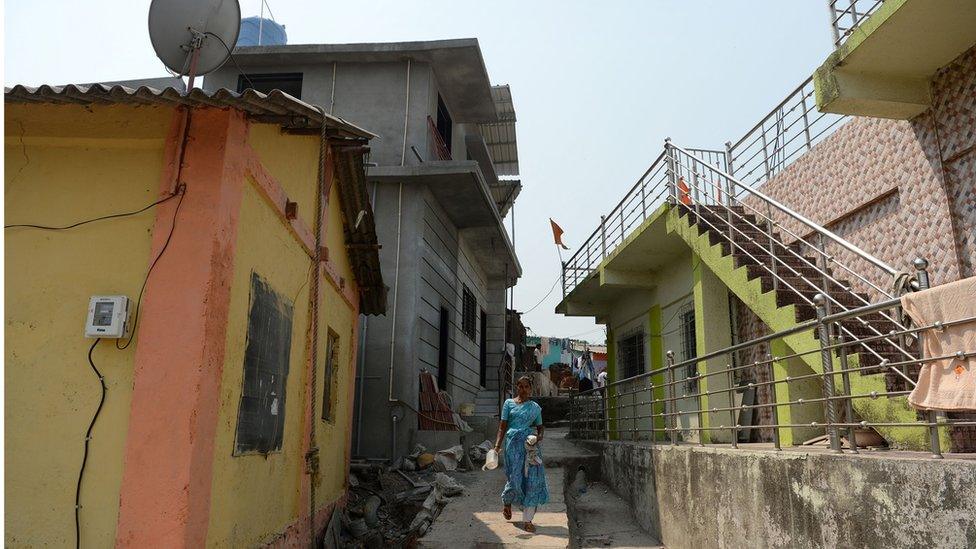 A woman walking past an alley in a village after electricity mains were installed in houses for the first time.