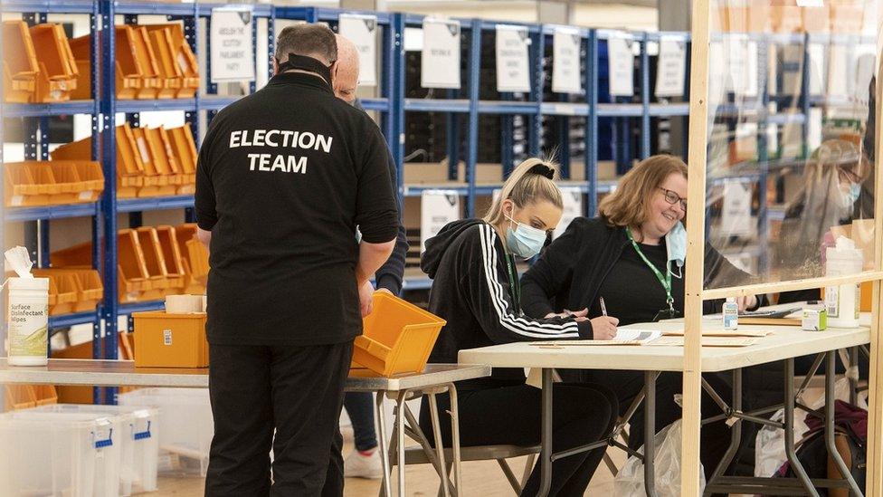 Vote counters in masks continue counting in Inverness, a man has his back turned with "Election Team" written on his T-shirt