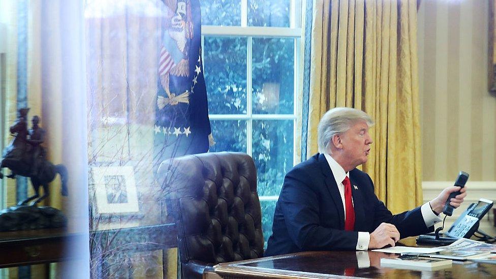 President Donald Trump is seen through a window making a phone call to King of Saudi Arabia, Salman bin Abd al-Aziz Al Saud, in the Oval Office of the White House, January 29, 2017