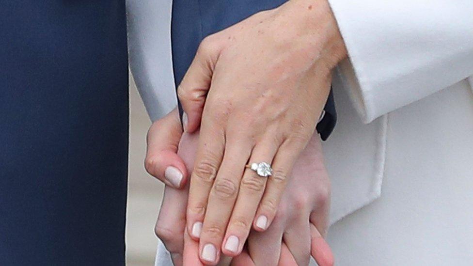 Harry and Meghan hold hands, showing the engagement rinng