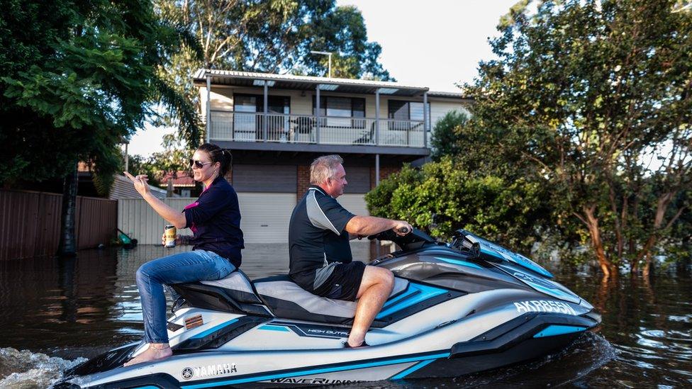 People are seen on a jet ski in a street affected by the flood on March 23, 2021 in Windsor, NSW