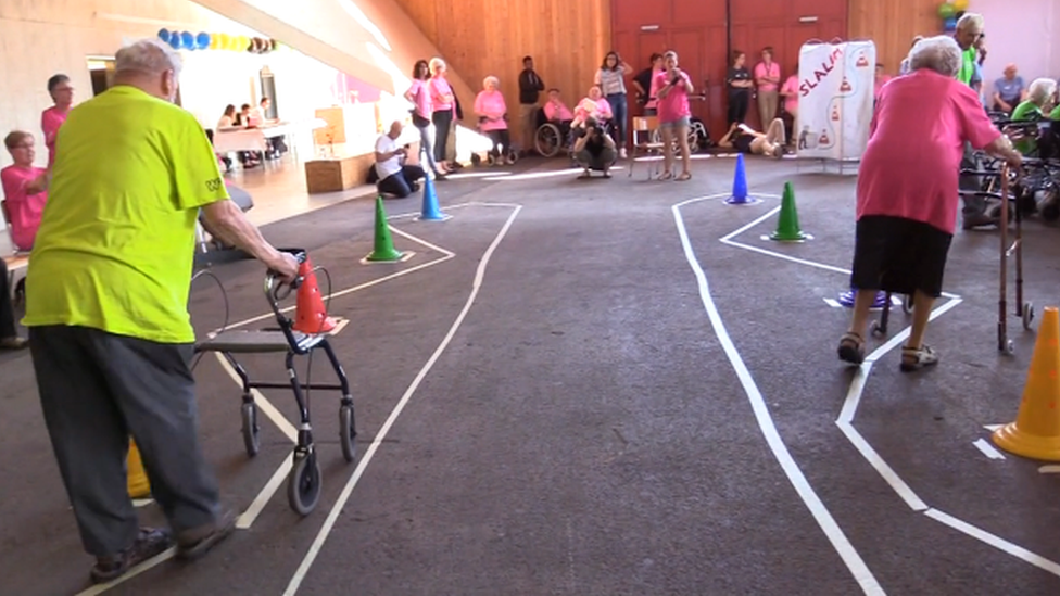 Two elderly people talking part in the walking-frame slalom