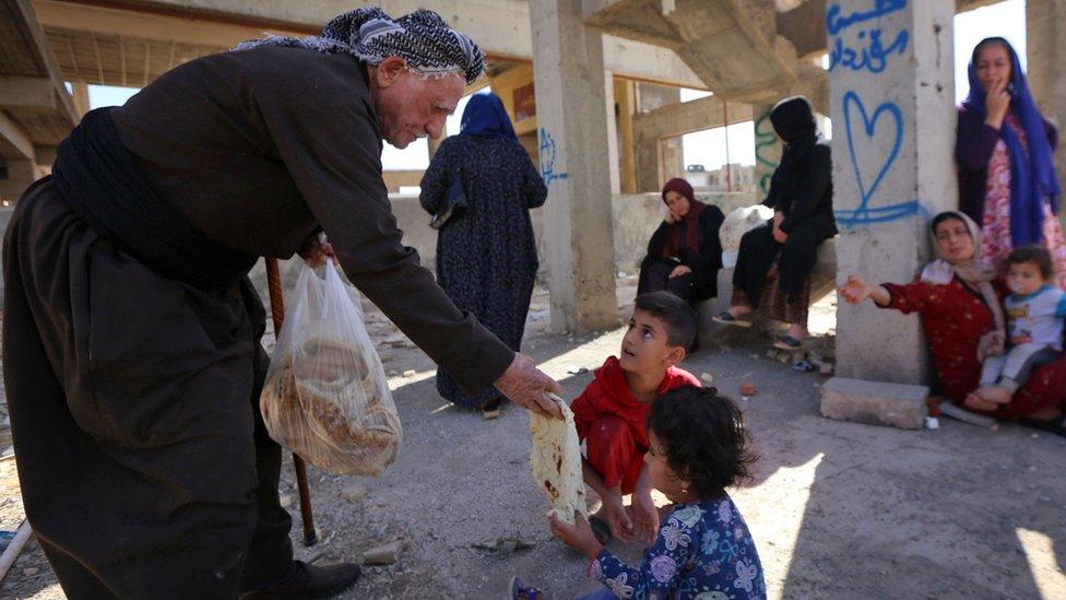 An Kurdish man distributes bread to a family of displaced people from Kirkuk province at a building site in Irbil, Iraq (19 October 2017)