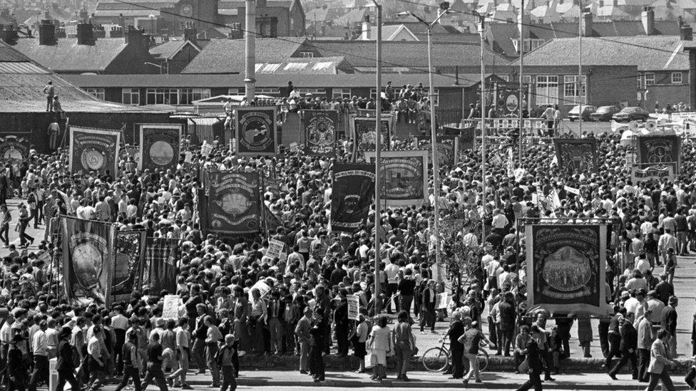 A large crowd carrying regional banners