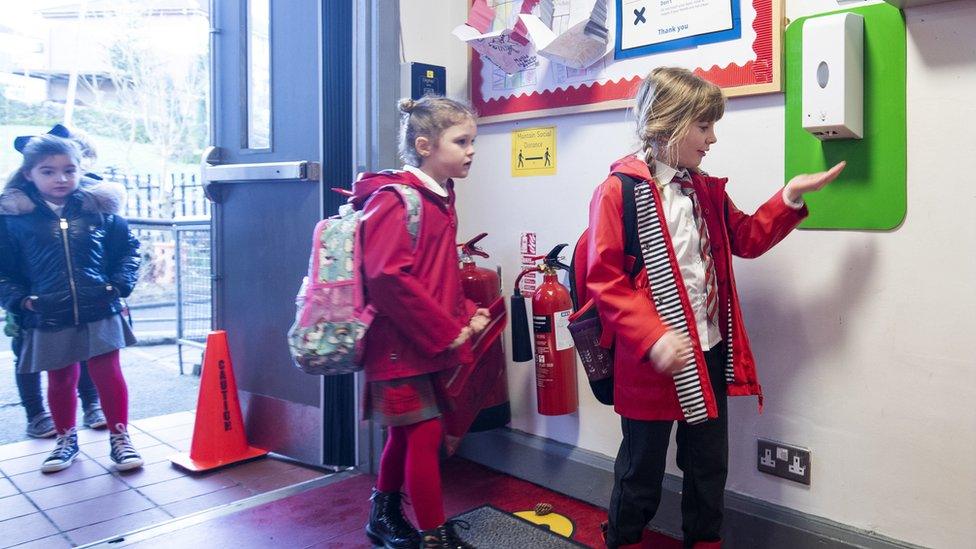 Children sanitise their hands on their way into school