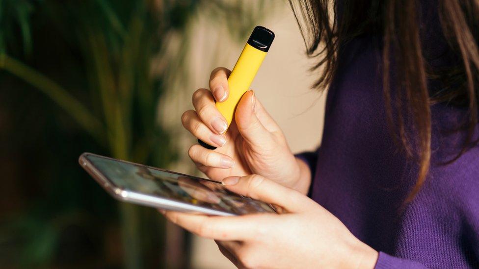 Young teen vaping while looking at her phone