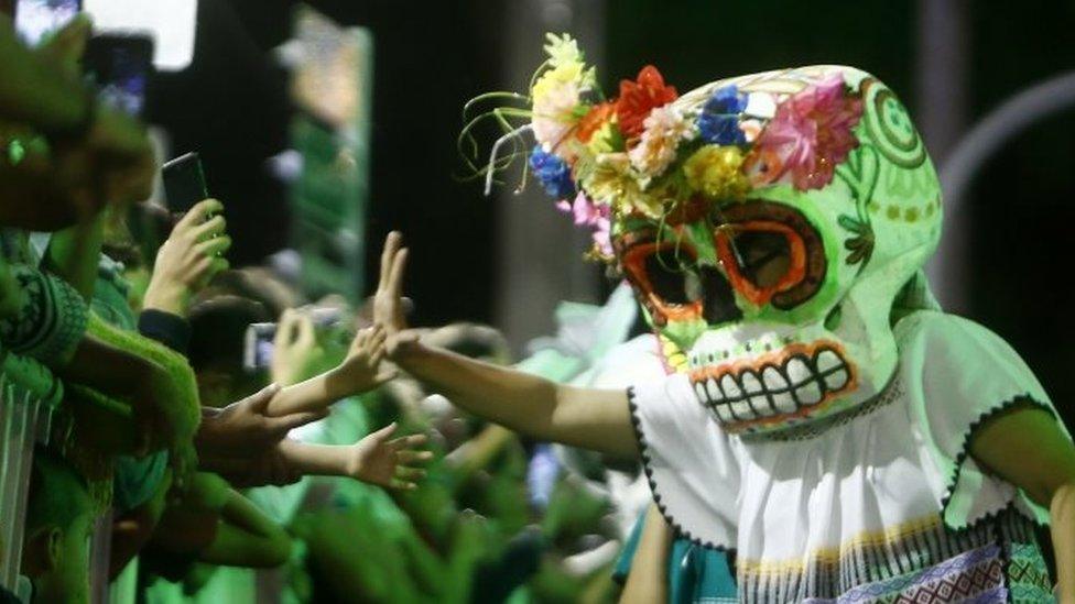 A performer with a papier-mache masks high-fives children watching the parade in Medellín