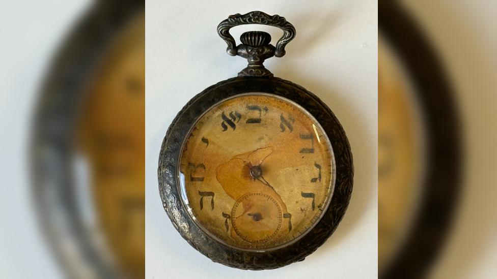 A rusted open-face pocket watch with faded Hebrew numerals and corroded hands