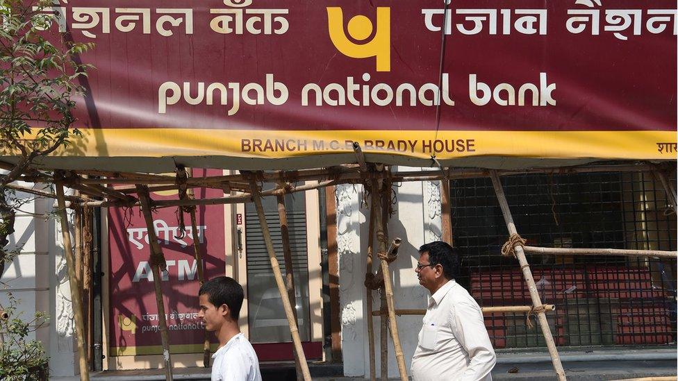 Indian men walk past signage for the state-owned Punjab National Bank (PNB) in Mumbai on February 14, 2018.