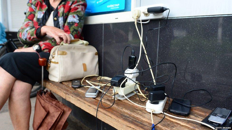 Residents wait as they charge their mobile phones at a kiosk with a rare working power outlet in the besieged city of Slavyansk on June 25, 2014