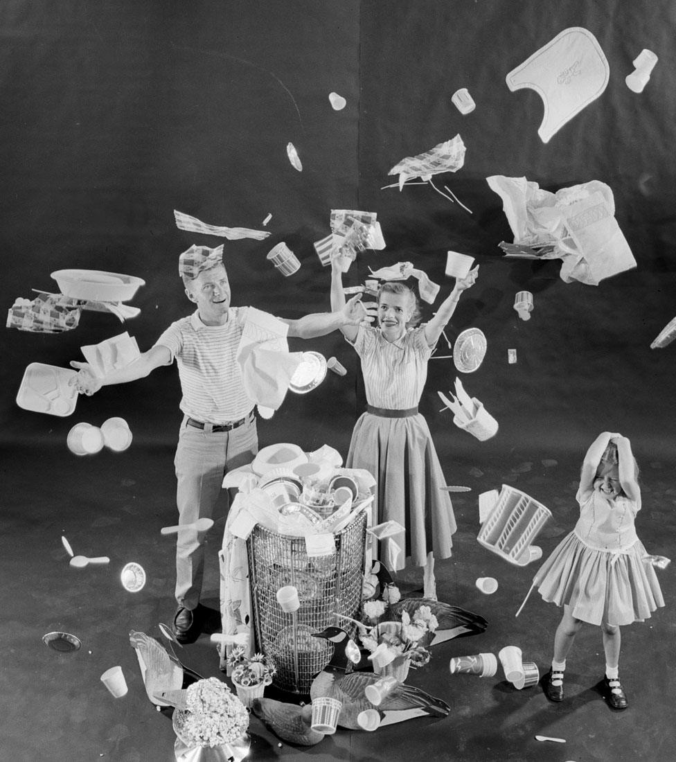 A smiling family fills a bin with various disposable goods