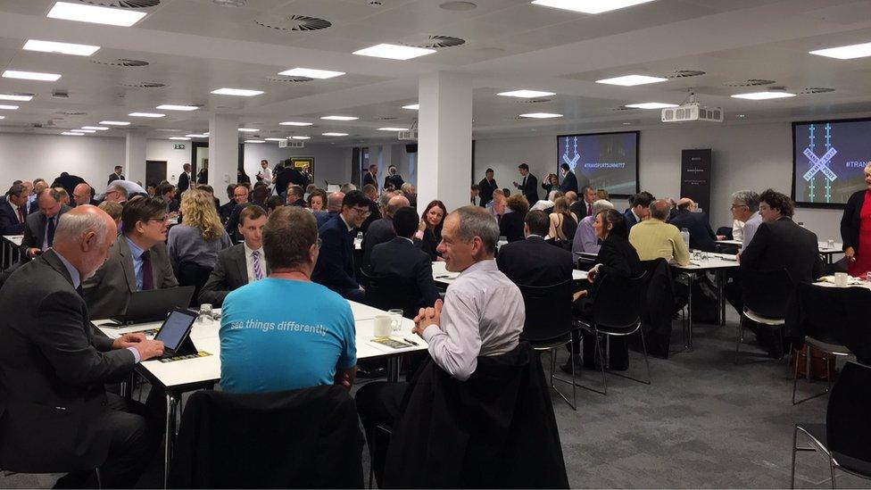 Men and women in suits sitting in a conference facing screens