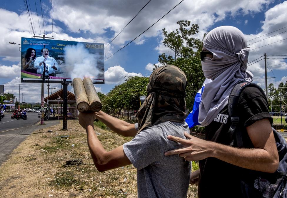 Masked students fire their home-made mortars at a big poster of President Daniel Ortega and his wife, Vice-President Rosario Murillo