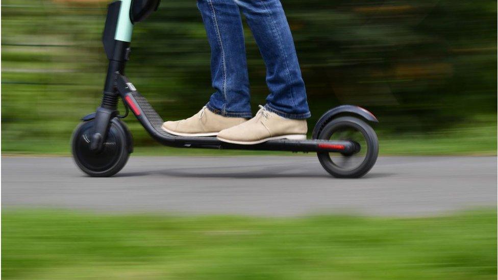 Man rides e-scooter in front of foliage