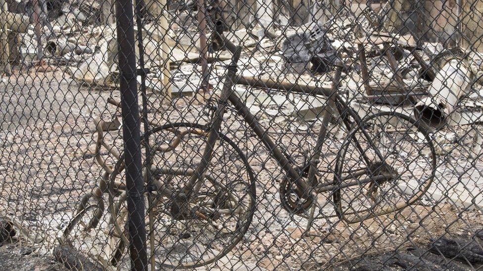 A charred bicycle leaning against a blackened fence