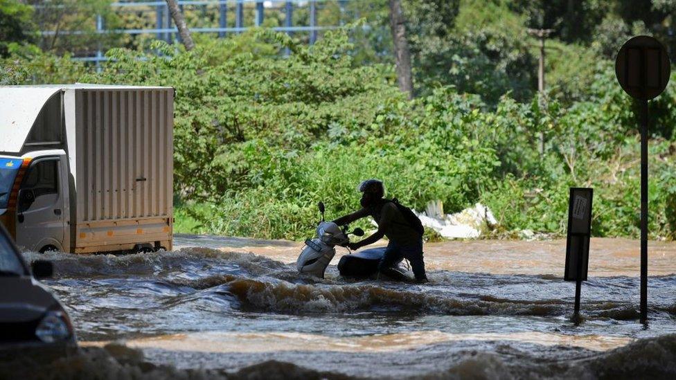 Motorists and vehicles wade through a street after heavy monsoon rains in Bangalore on September 5, 2022